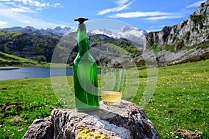 Green bottle and glass of natural Asturian cider made fromÂ fermented apples with view on Covadonga lake and tops of Picos de